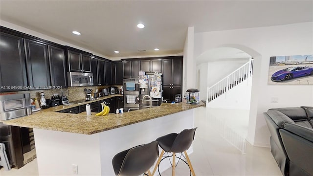 kitchen with a breakfast bar, backsplash, light stone countertops, kitchen peninsula, and stainless steel appliances