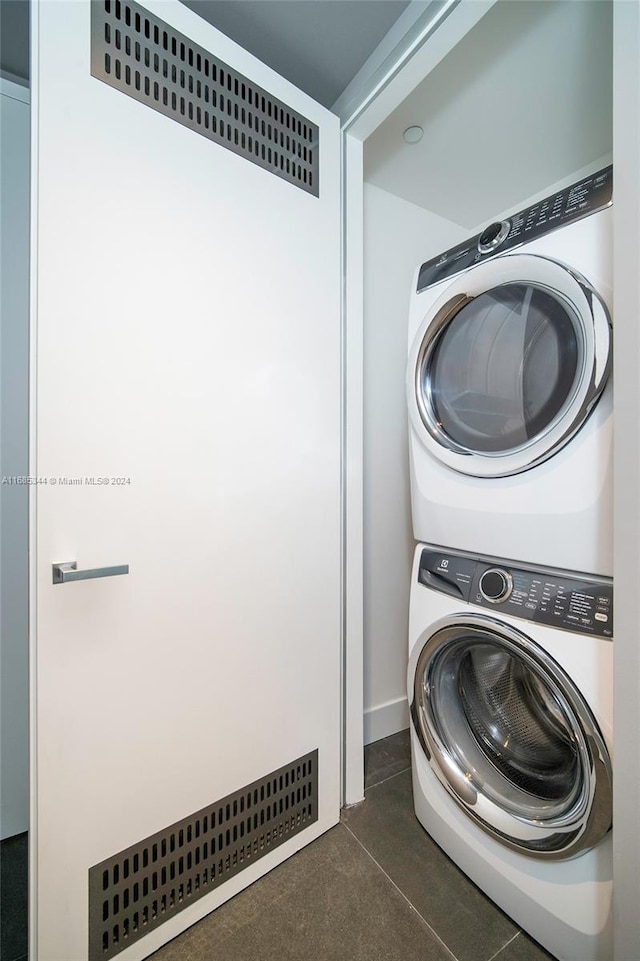 clothes washing area featuring dark tile patterned flooring and stacked washer and clothes dryer