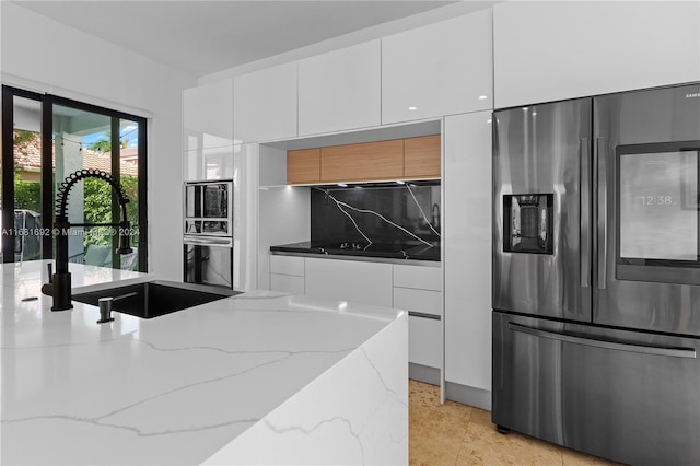 kitchen with sink, white cabinetry, appliances with stainless steel finishes, light stone counters, and tasteful backsplash