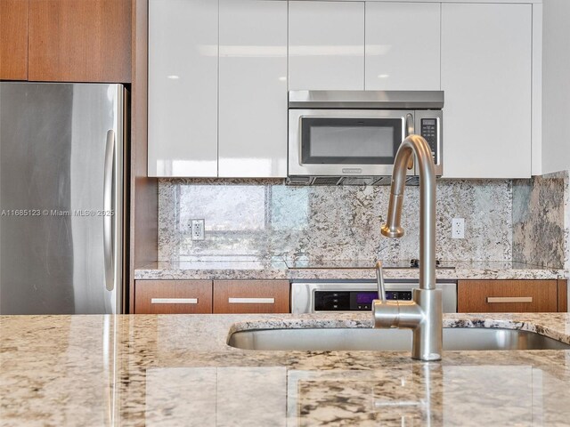 kitchen featuring light stone counters, stainless steel appliances, backsplash, and white cabinets