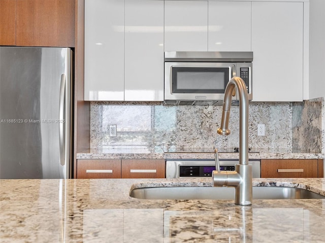 kitchen featuring light stone counters, stainless steel appliances, backsplash, and white cabinets