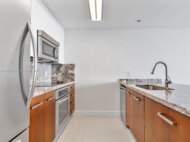 kitchen with light stone counters, stainless steel appliances, sink, and white cabinets