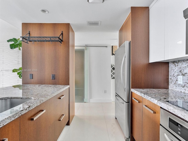 kitchen featuring light stone counters, appliances with stainless steel finishes, light tile patterned flooring, and backsplash