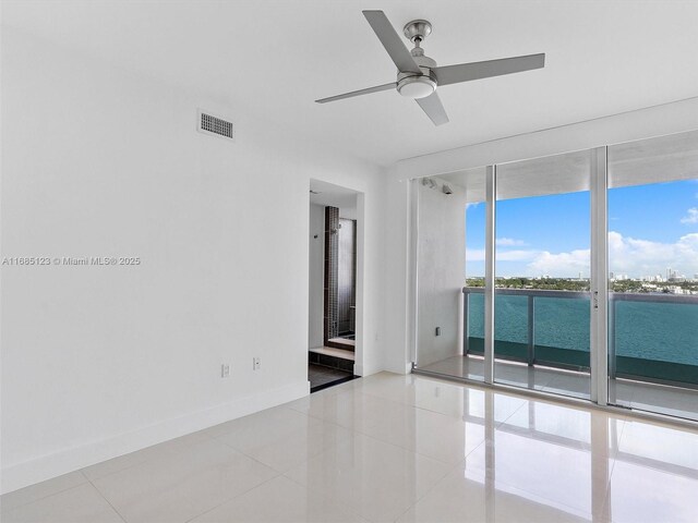 spare room featuring a water view, ceiling fan, light tile patterned floors, and floor to ceiling windows