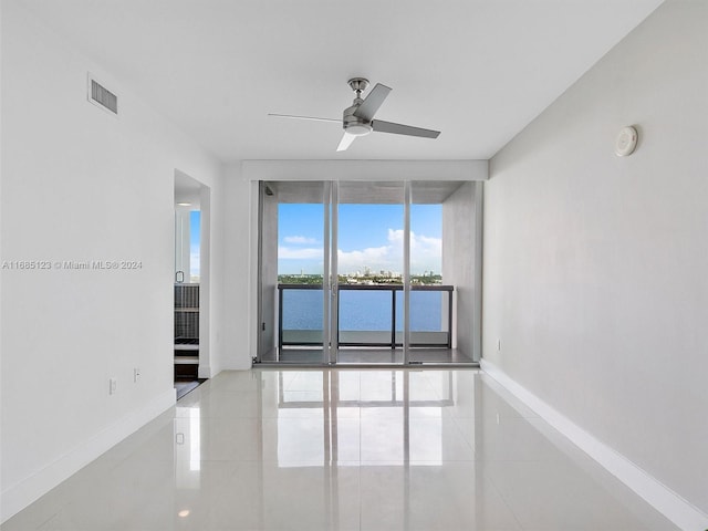 tiled empty room with a water view, ceiling fan, and floor to ceiling windows