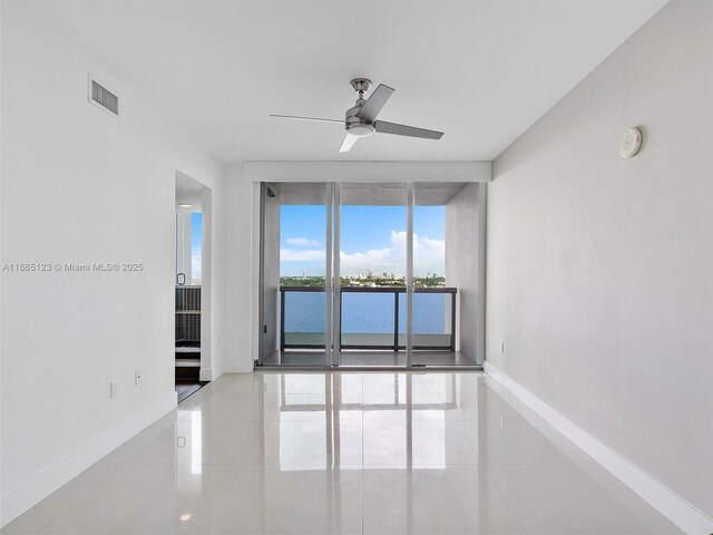 empty room featuring a water view, ceiling fan, and light tile patterned floors