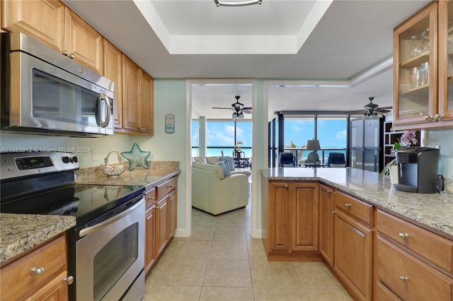 kitchen with light stone counters, a raised ceiling, appliances with stainless steel finishes, and light tile patterned floors