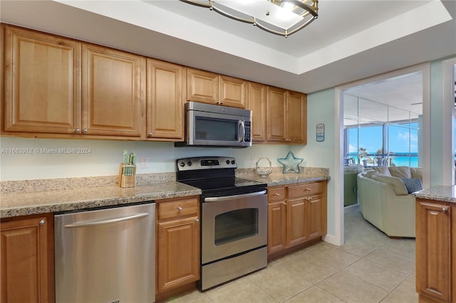 kitchen with light stone counters, a raised ceiling, appliances with stainless steel finishes, and light tile patterned floors