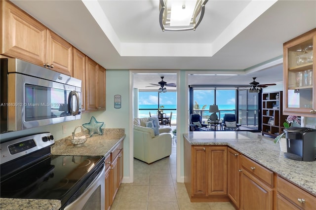 kitchen with light stone countertops, appliances with stainless steel finishes, a tray ceiling, and light tile patterned floors