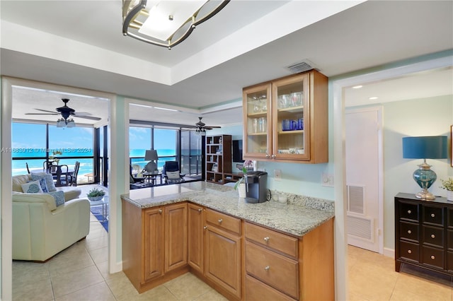 kitchen with light tile patterned flooring, light stone counters, a tray ceiling, and a water view