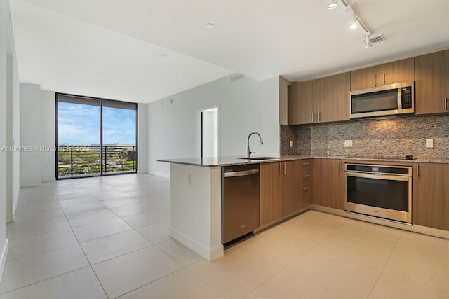 kitchen featuring kitchen peninsula, backsplash, appliances with stainless steel finishes, dark stone counters, and sink