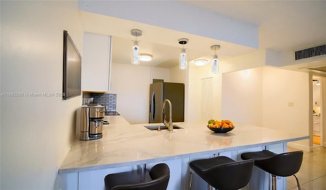 kitchen featuring a sink, white cabinetry, freestanding refrigerator, light stone countertops, and pendant lighting