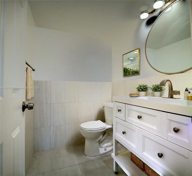 bathroom with a wainscoted wall, tile walls, toilet, vanity, and tile patterned flooring