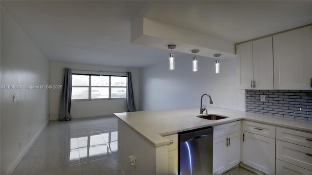 kitchen featuring a peninsula, stainless steel dishwasher, a sink, and white cabinets