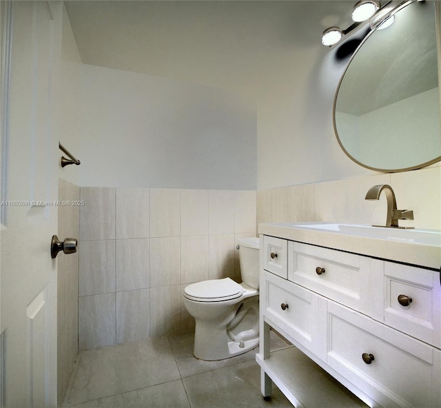 bathroom with tile walls, toilet, wainscoting, vanity, and tile patterned floors