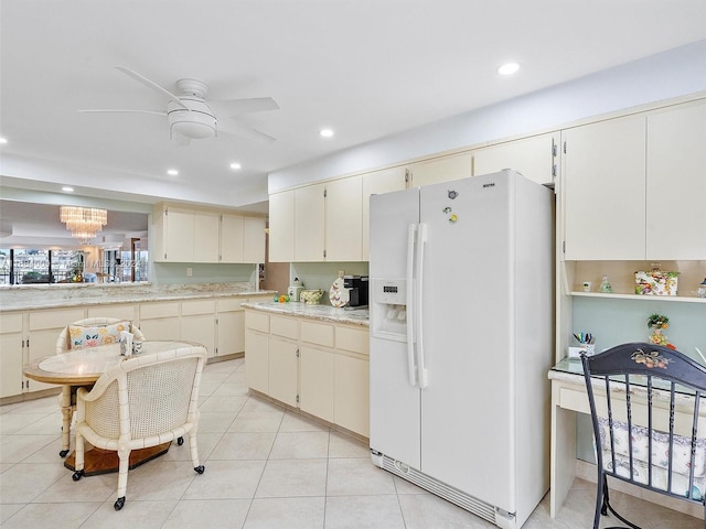 kitchen featuring cream cabinetry, light tile patterned floors, white refrigerator with ice dispenser, and ceiling fan with notable chandelier