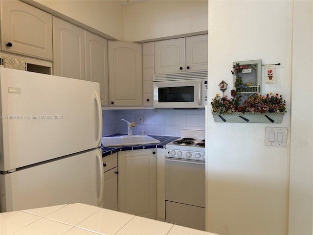 kitchen featuring tasteful backsplash, white cabinetry, tile counters, sink, and white appliances