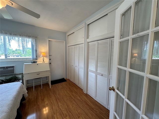 bedroom with hardwood / wood-style floors, a wall unit AC, two closets, and ceiling fan