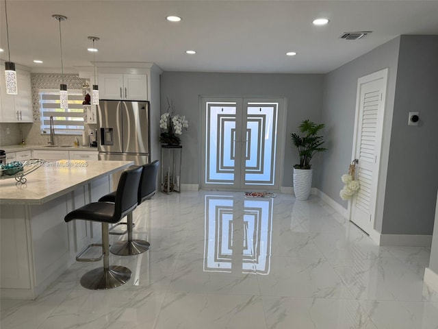 kitchen featuring pendant lighting, tasteful backsplash, white cabinets, and stainless steel refrigerator with ice dispenser