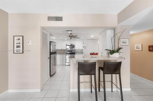 kitchen with kitchen peninsula, a breakfast bar area, decorative backsplash, white cabinets, and appliances with stainless steel finishes