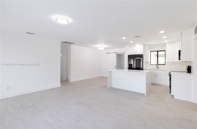 kitchen with sink, a barn door, a kitchen island, black refrigerator with ice dispenser, and white cabinetry