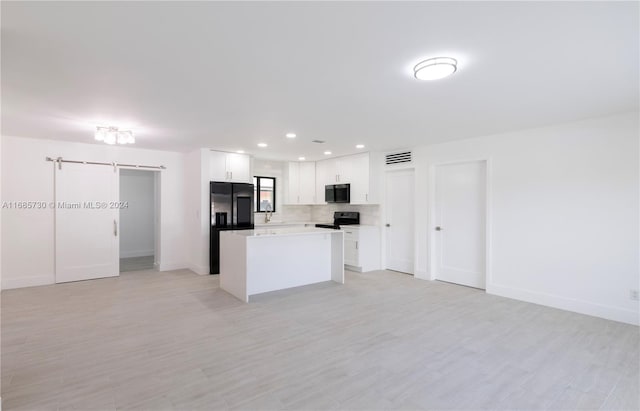 kitchen featuring white cabinets, backsplash, a barn door, black appliances, and a center island