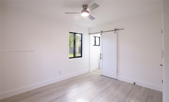 empty room featuring a barn door, light wood-type flooring, and ceiling fan