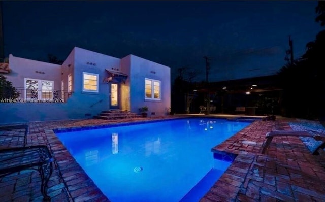 pool at night featuring a patio area