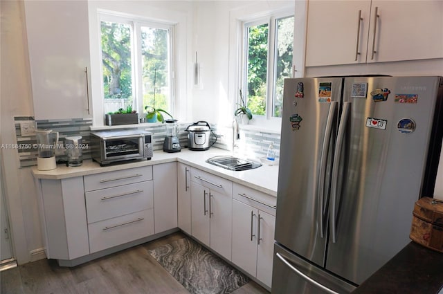 kitchen with stainless steel refrigerator, a wealth of natural light, hardwood / wood-style floors, and white cabinets