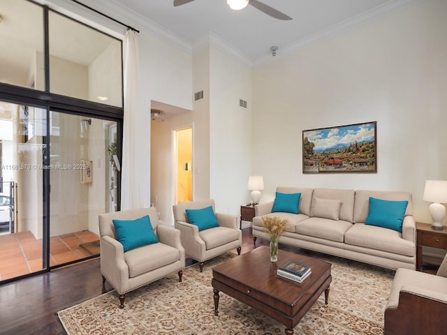 living room featuring hardwood / wood-style flooring, ornamental molding, ceiling fan, and a towering ceiling