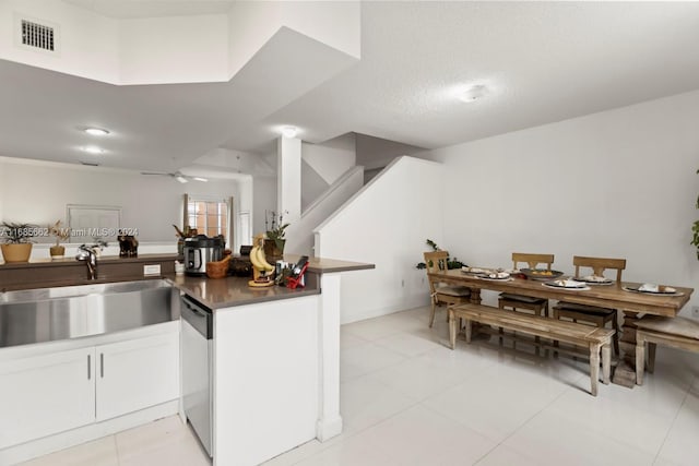 kitchen with kitchen peninsula, sink, light tile patterned floors, stainless steel dishwasher, and white cabinetry