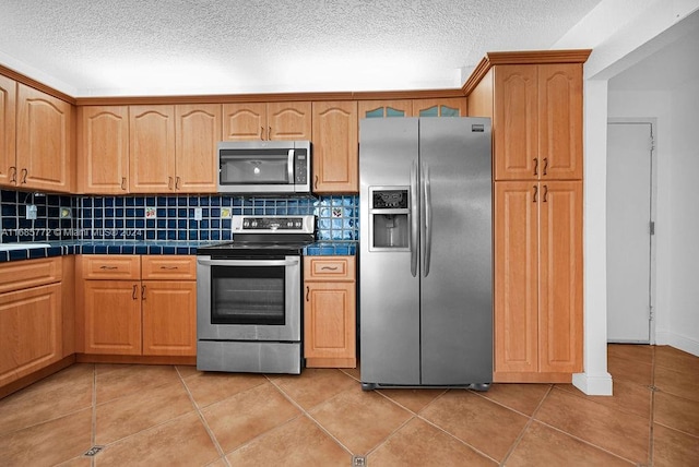 kitchen featuring light tile patterned floors, tile countertops, backsplash, a textured ceiling, and stainless steel appliances