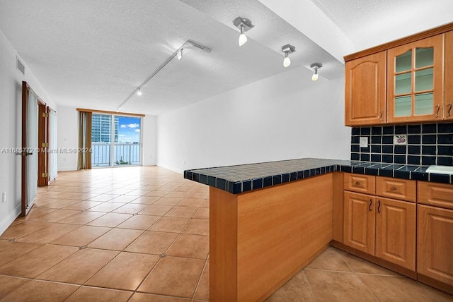 kitchen with track lighting, tile counters, kitchen peninsula, backsplash, and a textured ceiling