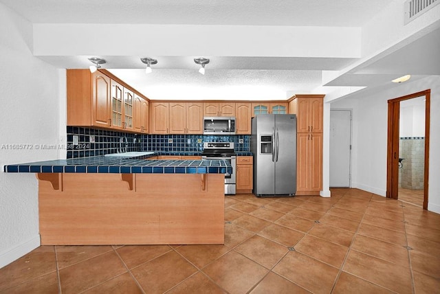 kitchen with tile countertops, stainless steel appliances, kitchen peninsula, and a kitchen breakfast bar