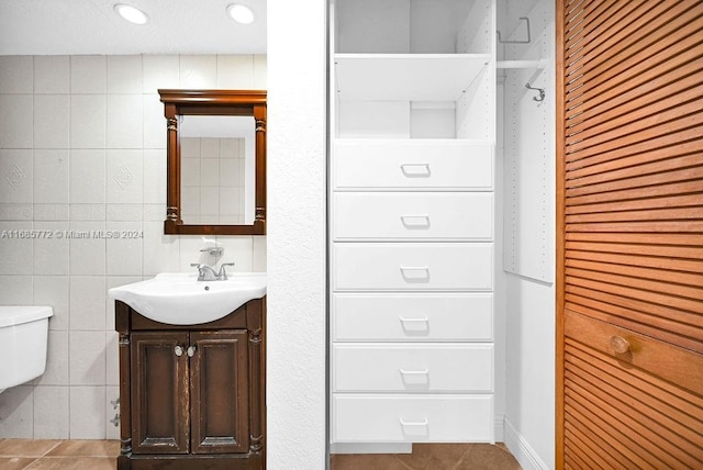 bathroom with toilet, vanity, tile walls, and tile patterned flooring