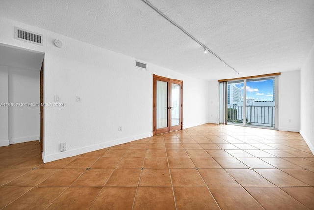 empty room featuring french doors, a textured ceiling, light tile patterned floors, and floor to ceiling windows