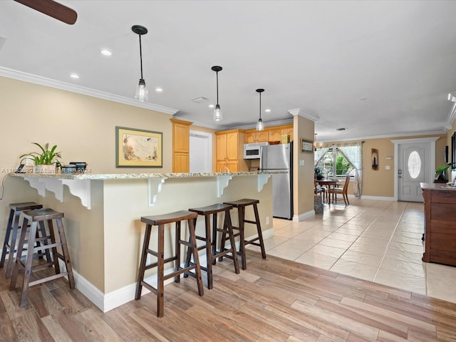 kitchen with a breakfast bar, stainless steel fridge, hanging light fixtures, and light wood-type flooring