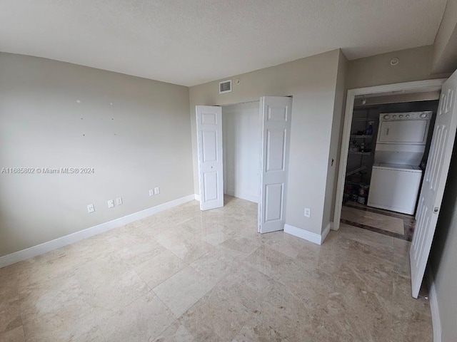 unfurnished bedroom featuring a textured ceiling and stacked washer / dryer