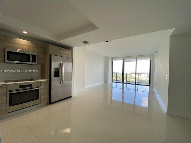 kitchen with a raised ceiling, appliances with stainless steel finishes, light tile patterned floors, and floor to ceiling windows