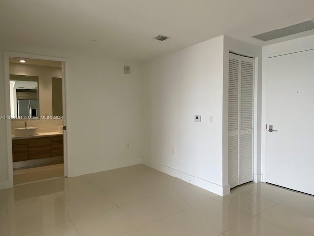 unfurnished bedroom featuring sink, light tile patterned flooring, a closet, and ensuite bath