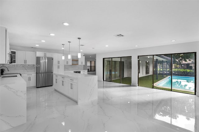 kitchen with stainless steel fridge, white cabinetry, sink, pendant lighting, and light stone counters