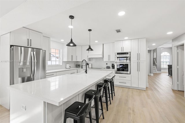 kitchen with white cabinetry, a center island with sink, a healthy amount of sunlight, and appliances with stainless steel finishes