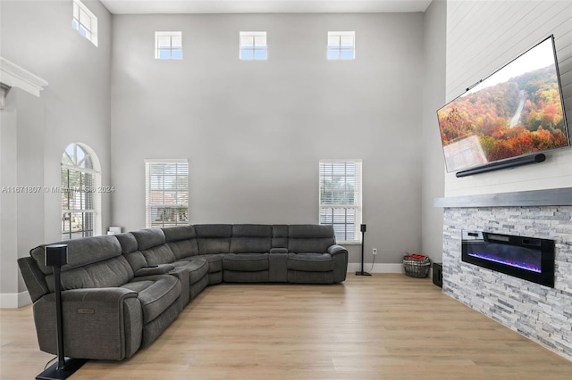 living room featuring light wood-type flooring, a towering ceiling, and a stone fireplace