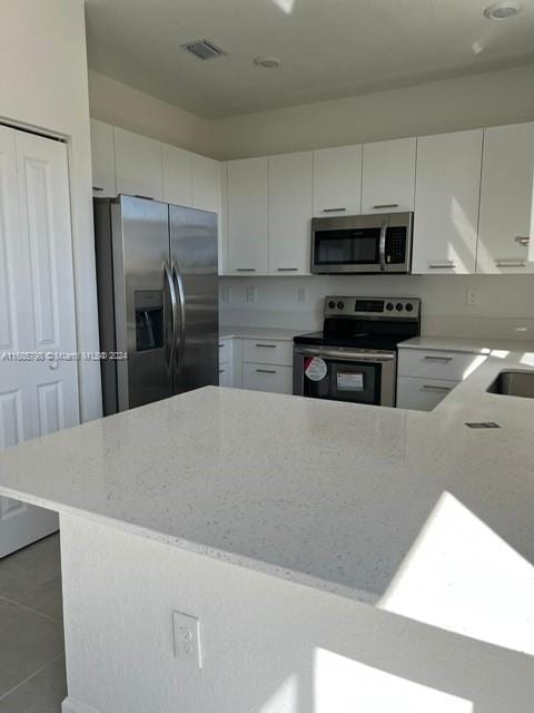 kitchen with white cabinetry, light stone counters, and stainless steel appliances