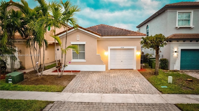 mediterranean / spanish-style house with a garage, decorative driveway, a tile roof, and stucco siding