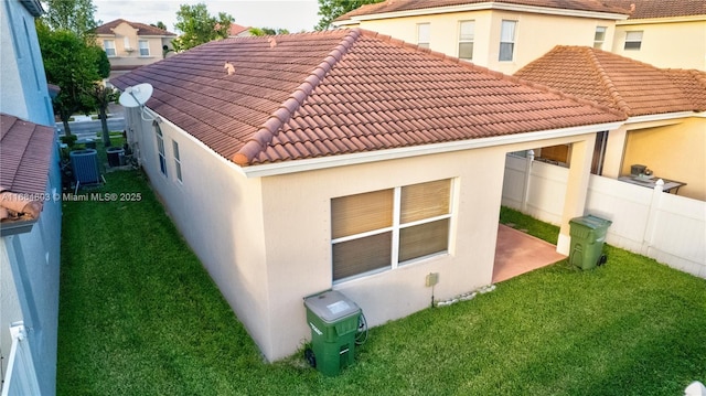 rear view of house with a tiled roof, a yard, fence, and stucco siding