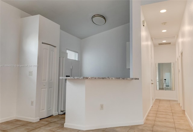 kitchen featuring light tile patterned floors, baseboards, visible vents, light stone counters, and white fridge