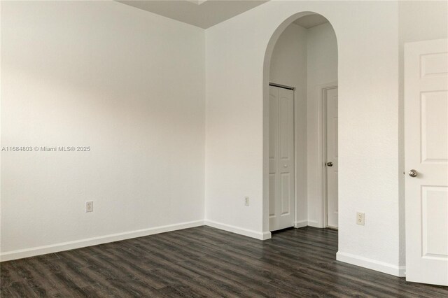 unfurnished room featuring baseboards, arched walkways, and dark wood-type flooring