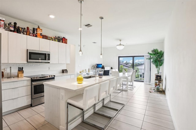 kitchen featuring a kitchen bar, hanging light fixtures, stainless steel appliances, white cabinets, and a center island with sink