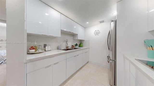 kitchen featuring decorative backsplash, light tile patterned floors, sink, white cabinetry, and stainless steel fridge